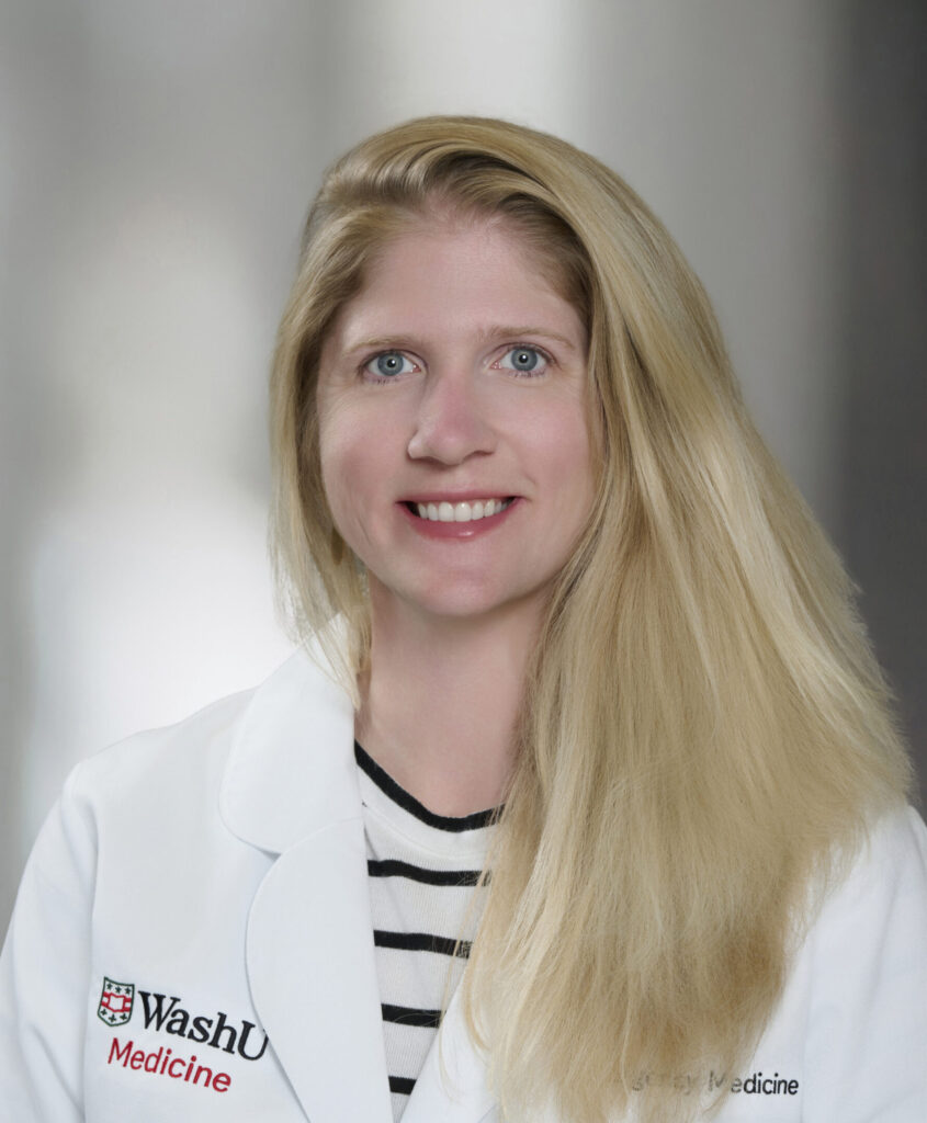 A woman with long blonde hair, wearing a white medical coat with the WashU Medicine logo and a black-and-white striped shirt, smiles at the camera against a blurred gray background.